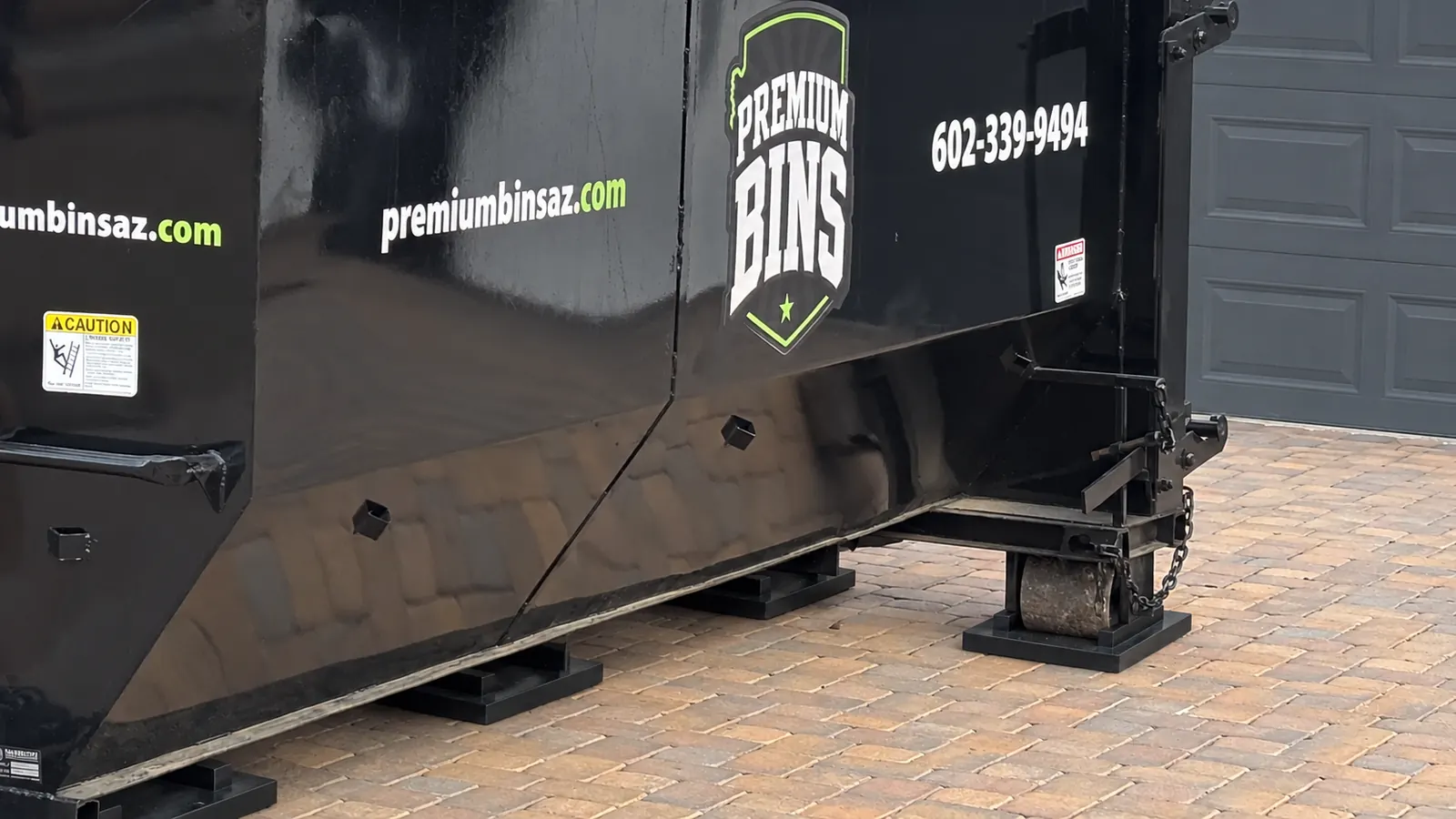 Driveway protector pads under the rollers and rails of a Premium Bins dumpster on pavers